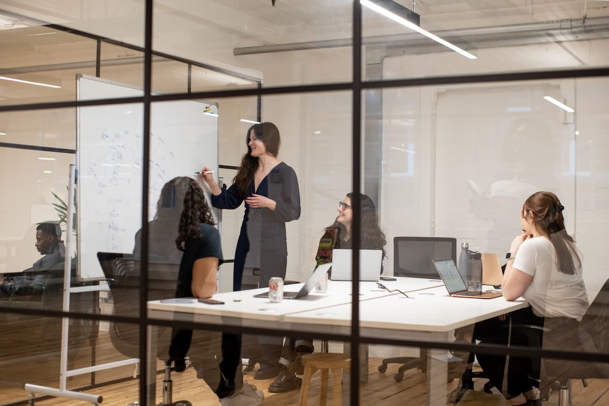 Picture through a meeting room glass wall with a group of people discussing a white board presentation